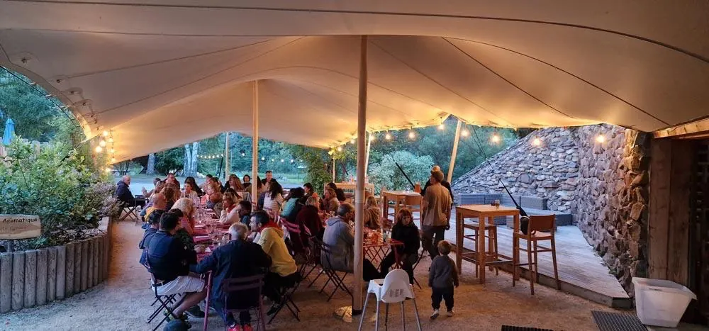 Événement sous toile tendue sur une terrasse en bois, invités attablés en soirée