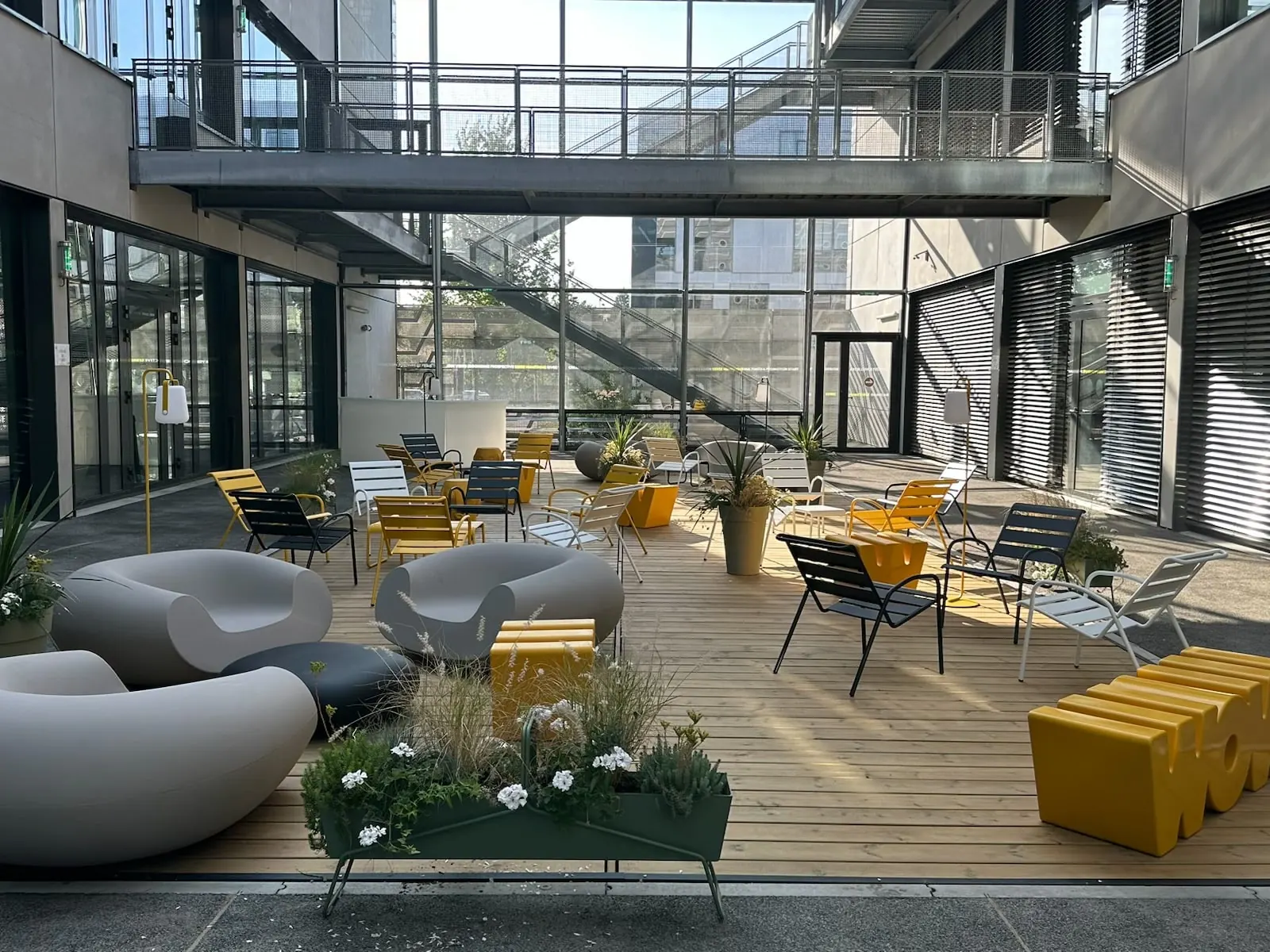 Patio d'entreprise aménagé par Marc Verde : terrasse bois, fauteuils, assises colorées et jardinières au cœur d'un bâtiment tertiaire